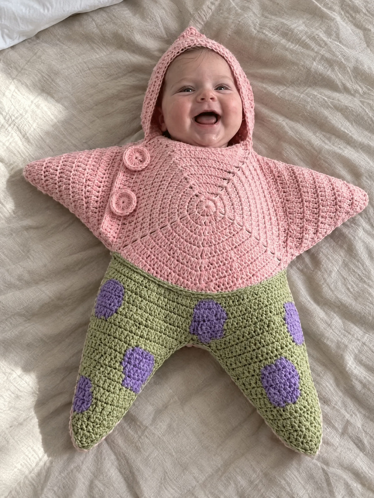 Hand-crocheted starfish suit in Pinky Green, on a baby